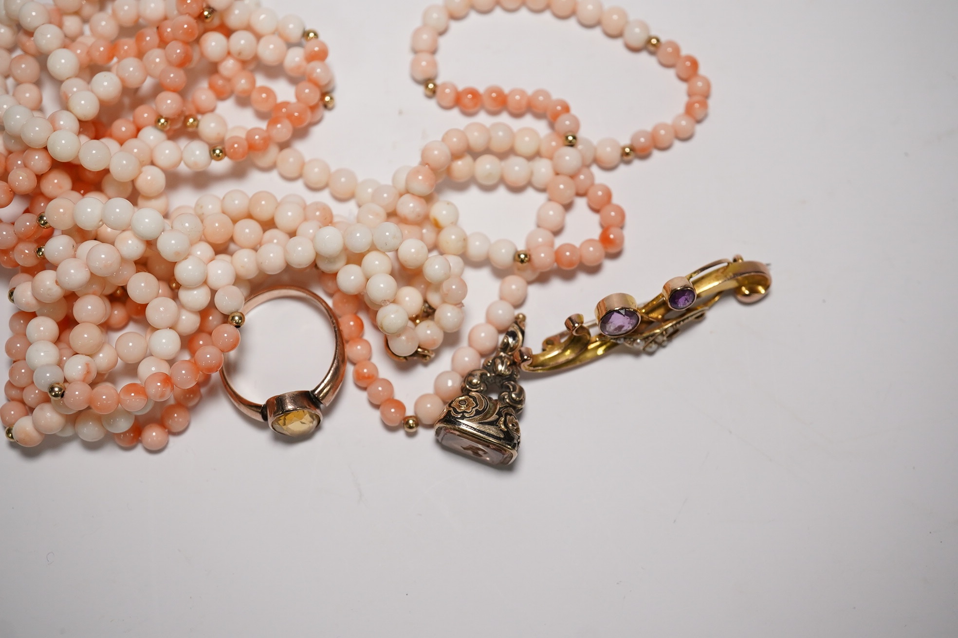 An Edwardian 9ct gold and gen set scroll brooch, 40mm, a yellow metal and gem set ring, a yellow metal overlaid fob seal and a modern coral bead necklace. Condition - poor to fair